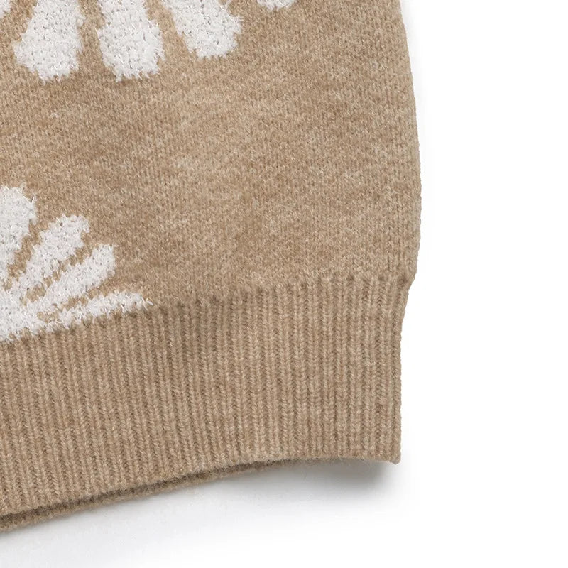 Close-up of a tan knit sweater with white daisy patterns, featuring a ribbed hem against a white background.