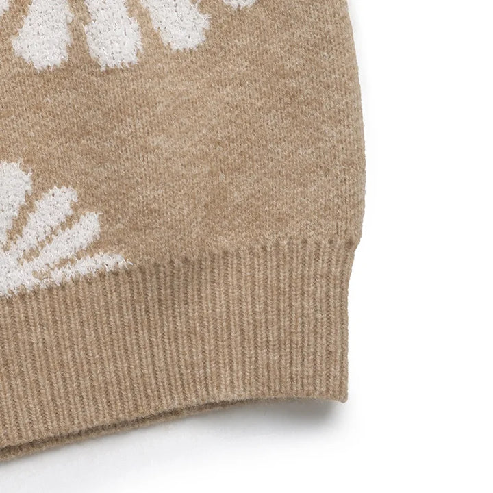 Close-up of a tan knit sweater with white daisy patterns, featuring a ribbed hem against a white background.
