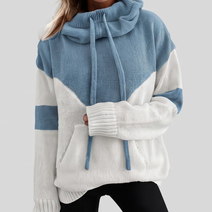 Woman wearing an oversized knit hoodie in blue and white color block with a drawstring cowl neck and front pocket.