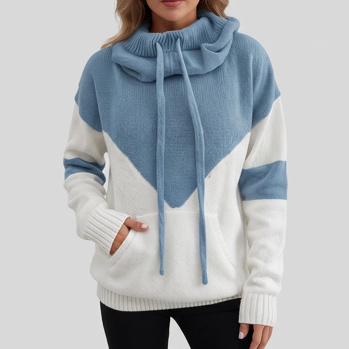 Woman wearing a textured blue and white color block knit hoodie with a cowl neck, drawstrings, and a front pocket.