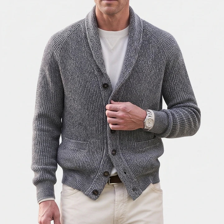 Man wearing a grey ribbed knit shawl collar cardigan with dark buttons, over a white tee and beige pants.