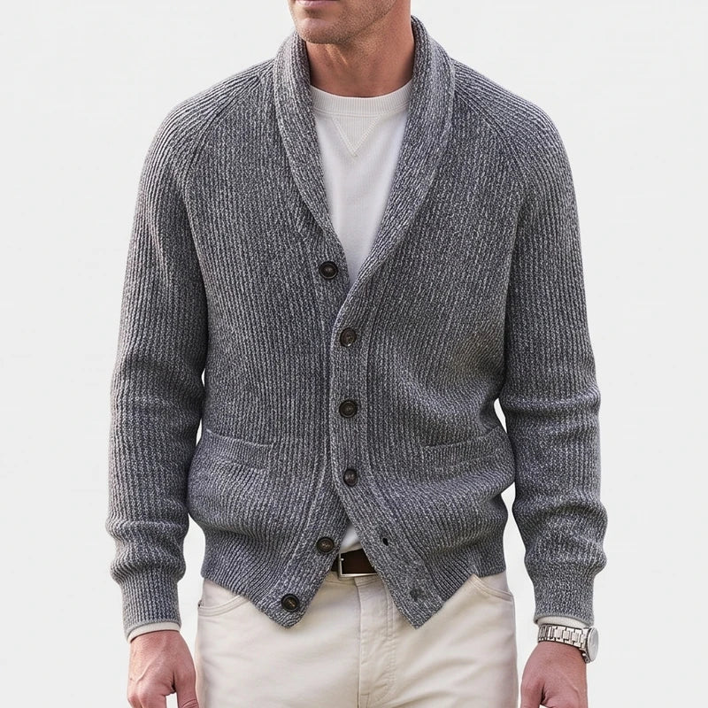 Man wearing a grey ribbed knit shawl collar cardigan over a white tee, with cream trousers and a brown belt.