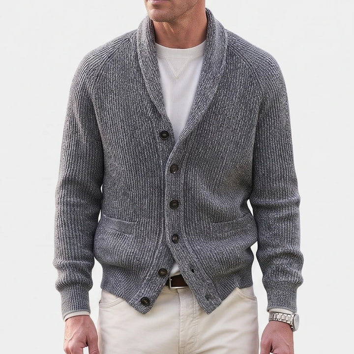 Man wearing a grey ribbed knit shawl collar cardigan over a white tee, with cream trousers and a brown belt.