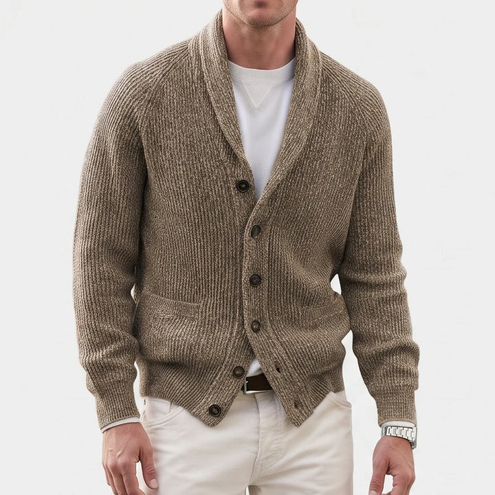 Man wearing a textured brown knit cardigan with a large shawl collar, five dark buttons, and front pockets, over a white tee.