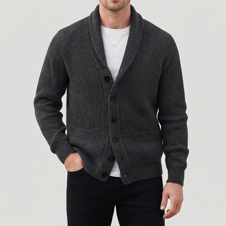 Man wearing a dark gray ribbed knit cardigan with a shawl collar, black buttons, and two front pockets.