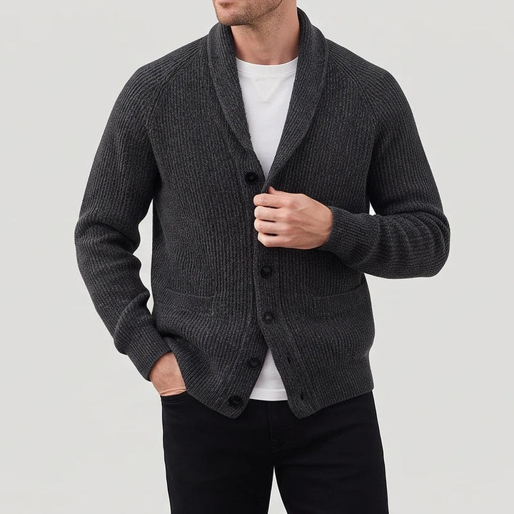 Man wearing a dark grey ribbed knit cardigan with a shawl collar, black buttons, and front pockets over a white tee.