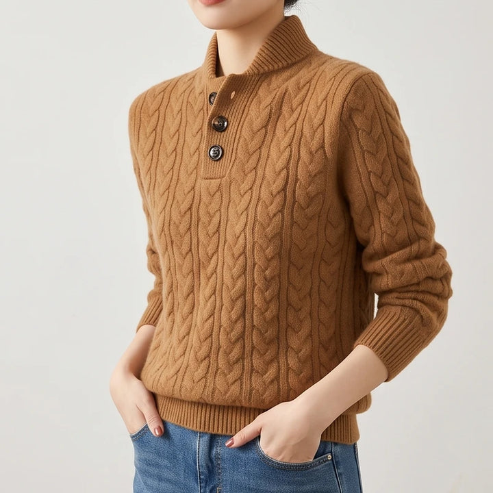 Woman wearing a brown cable knit sweater with a buttoned mock neck and ribbed hem, hands in blue jeans pockets.