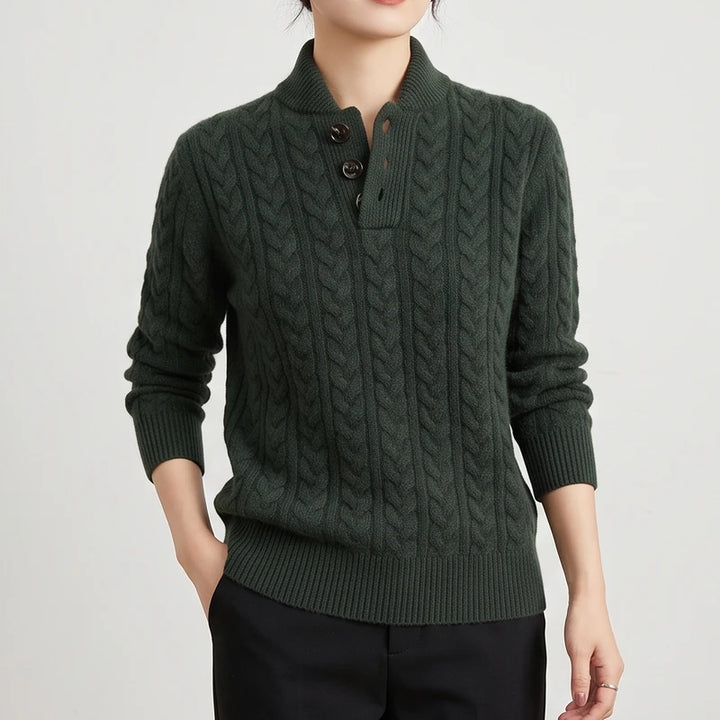 Woman wearing a dark green cable knit sweater with a stand collar and three dark brown buttons on the placket.