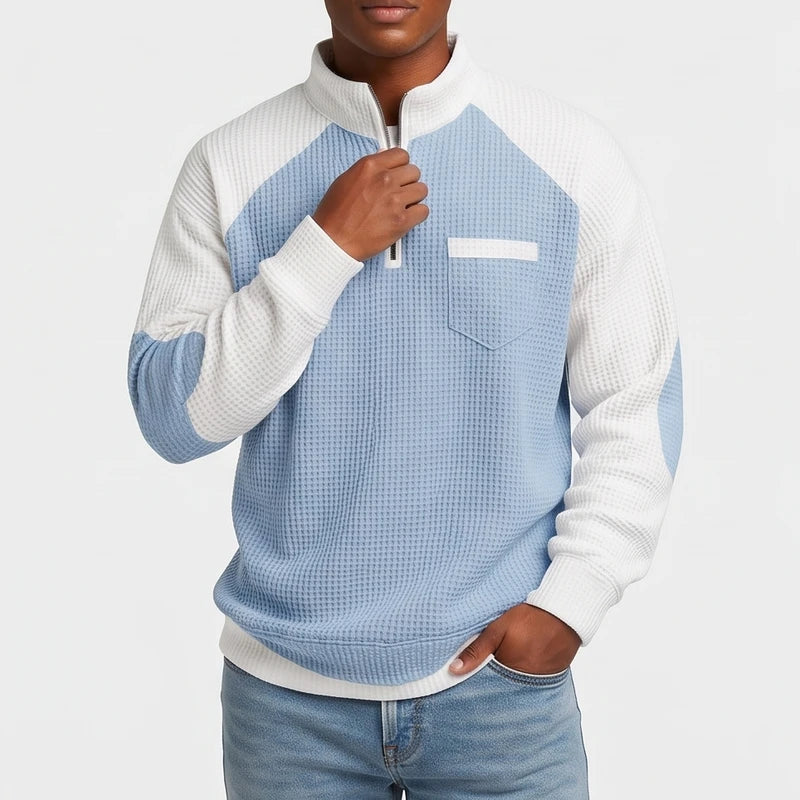 Man wearing a light blue and white waffle knit quarter-zip sweater with a chest pocket, holding the zipper.