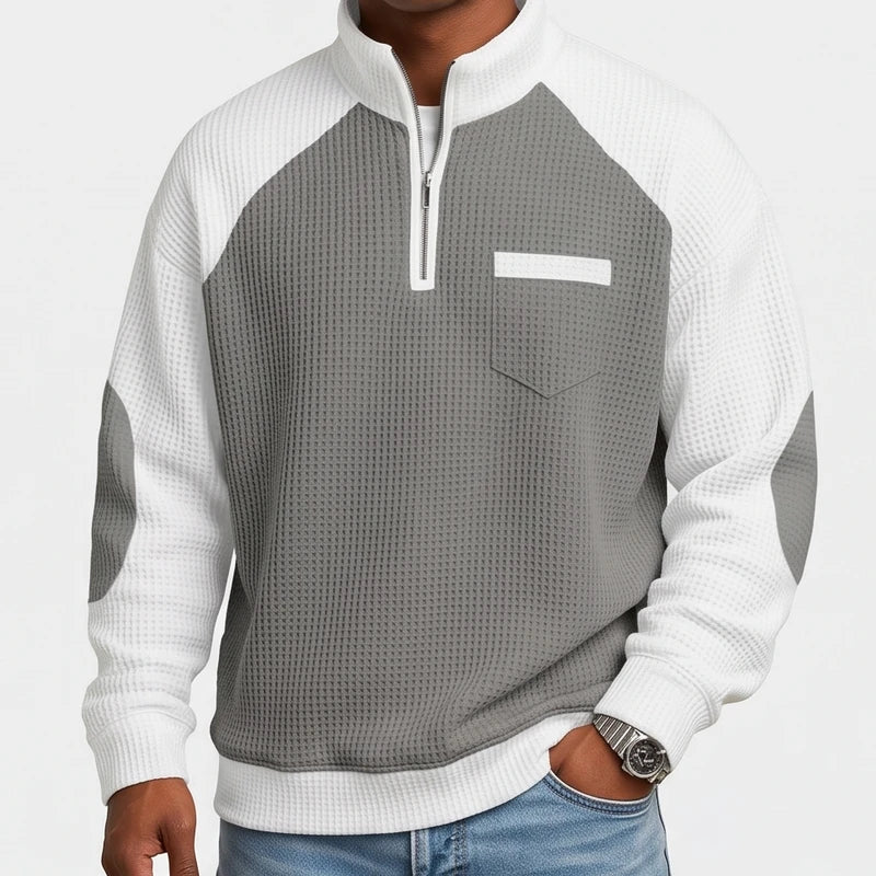 Man wearing a grey and white waffle knit half-zip sweater with a chest pocket and elbow patches.
