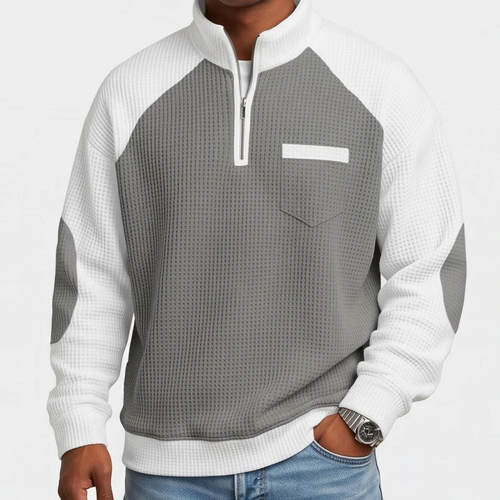 Man wearing a grey and white waffle knit half-zip sweater with a chest pocket and elbow patches.