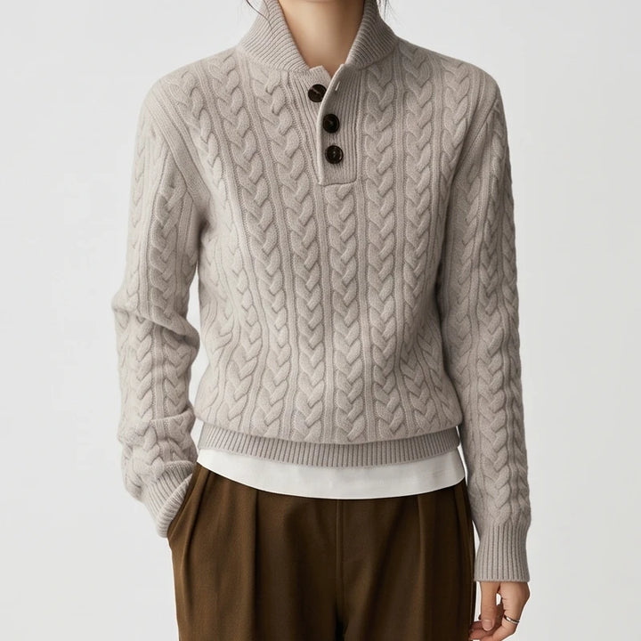 Woman wearing a light gray cable knit sweater with a shawl collar, three dark brown buttons, and ribbed cuffs.