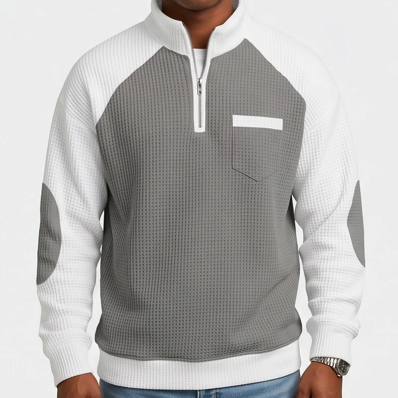 Man wearing a grey and white waffle knit quarter-zip sweater with elbow patches and a chest pocket, front view.