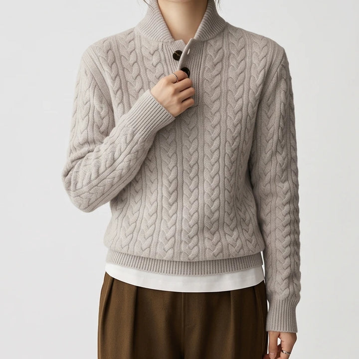 Woman wearing a light gray cable knit sweater with dark brown buttons on the shawl collar, over a white shirt.