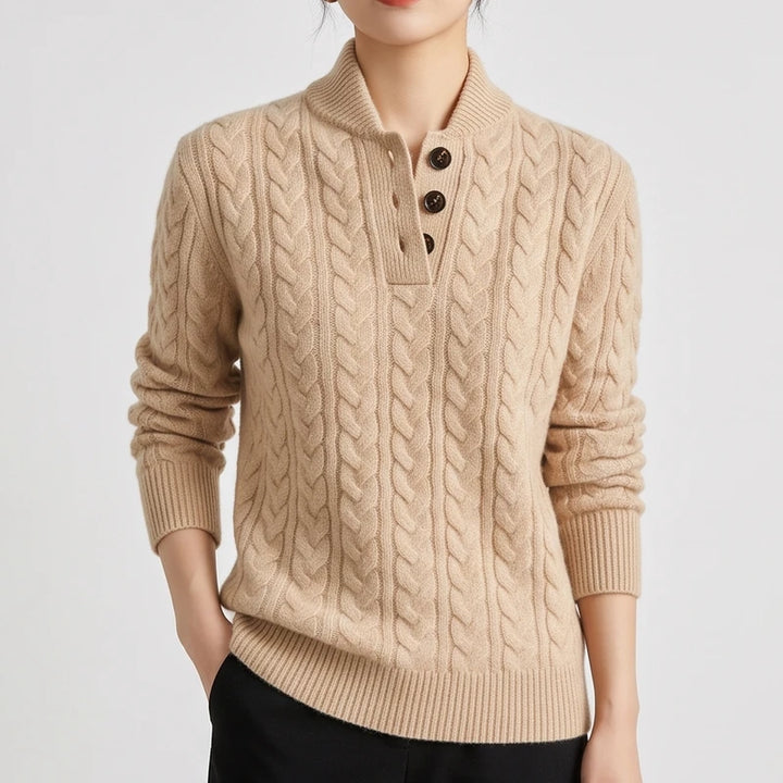 Woman wearing a beige cable knit sweater with a collar and three brown buttons on the placket, hands in black pants pockets.