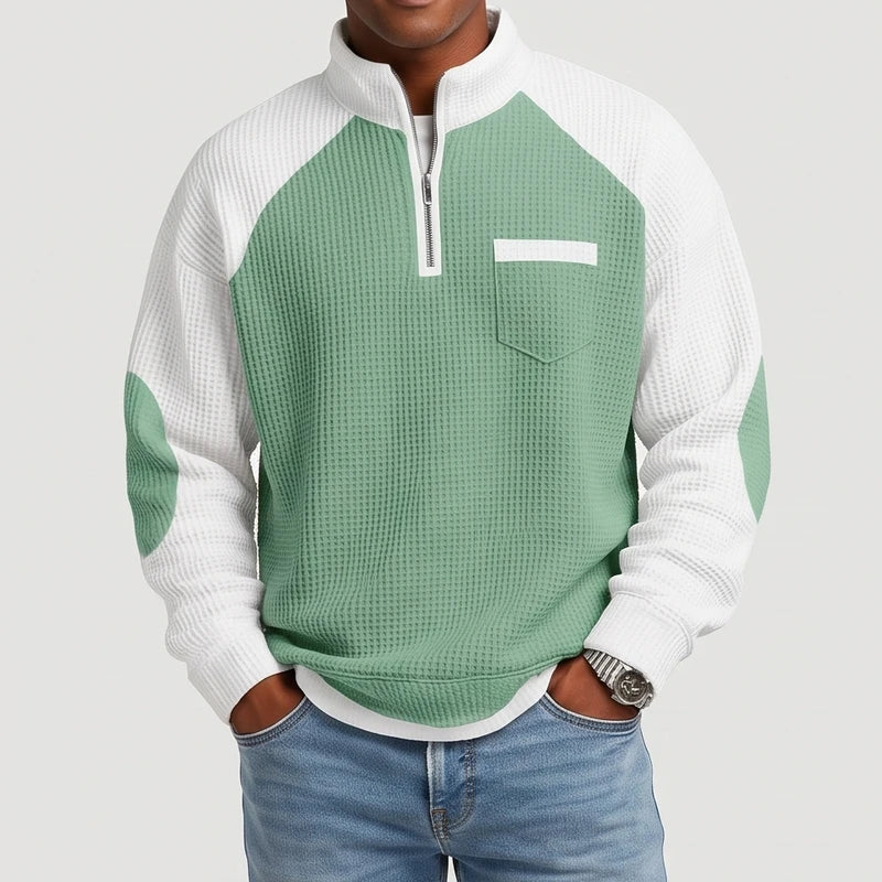 Man wearing a two-tone waffle knit sweater with a green body, white raglan sleeves, a half-zip, and a front pocket.