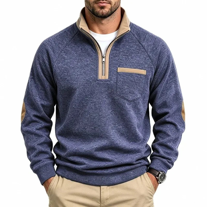 Man wearing a blue heathered knit sweatshirt with a tan quarter-zip collar, chest pocket, and elbow patches.
