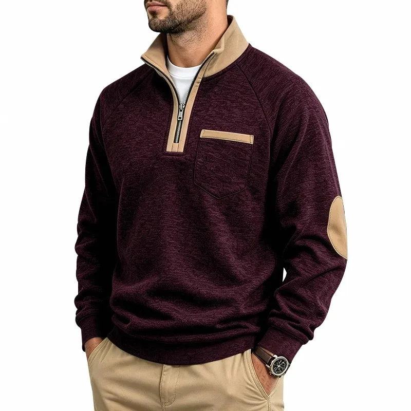 Man wearing a flecked maroon quarter-zip pullover with a tan collar, chest pocket trim, and elbow patches, with hands in khaki pants.