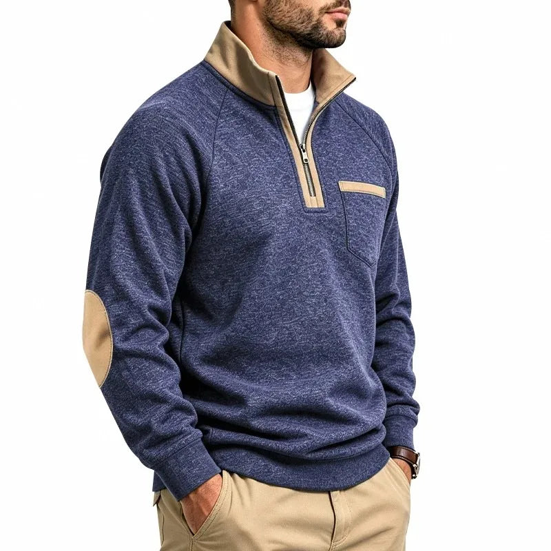Man wearing a blue knit sweatshirt with a tan quarter-zip collar, matching elbow patches, and chest pocket.