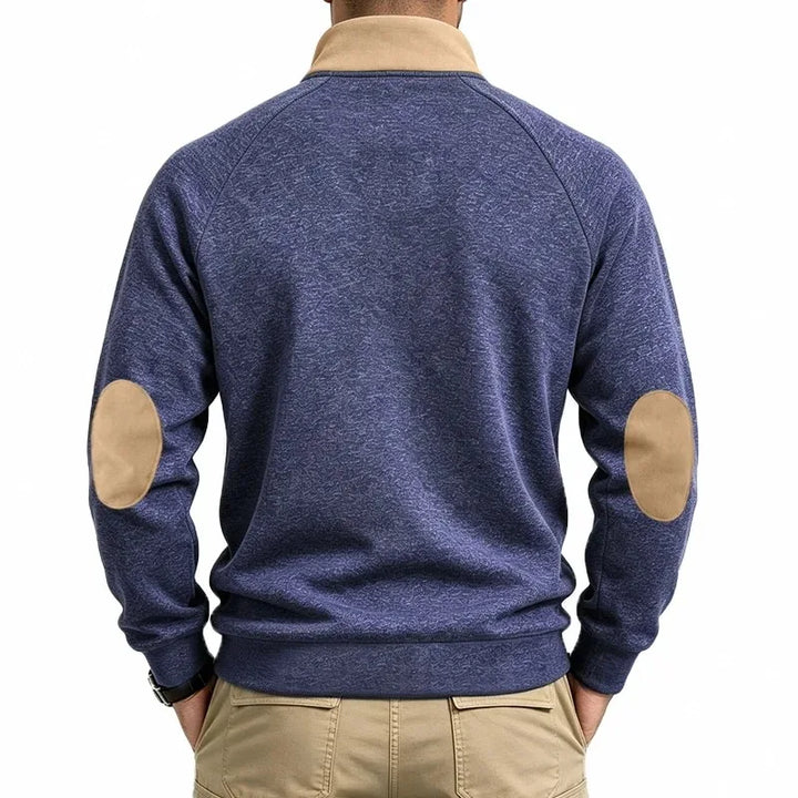 Man wearing a blue marled knit sweatshirt with tan collar and oval elbow patches, viewed from the back.