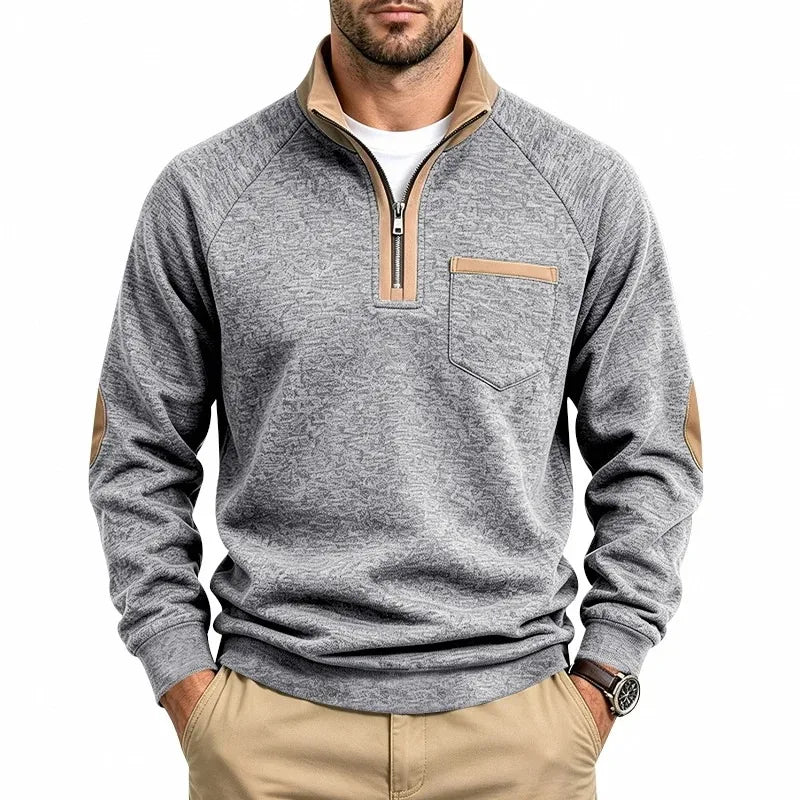 Man wearing a grey textured knit sweatshirt with a quarter-zip tan collar, tan chest pocket detail, and elbow patches.