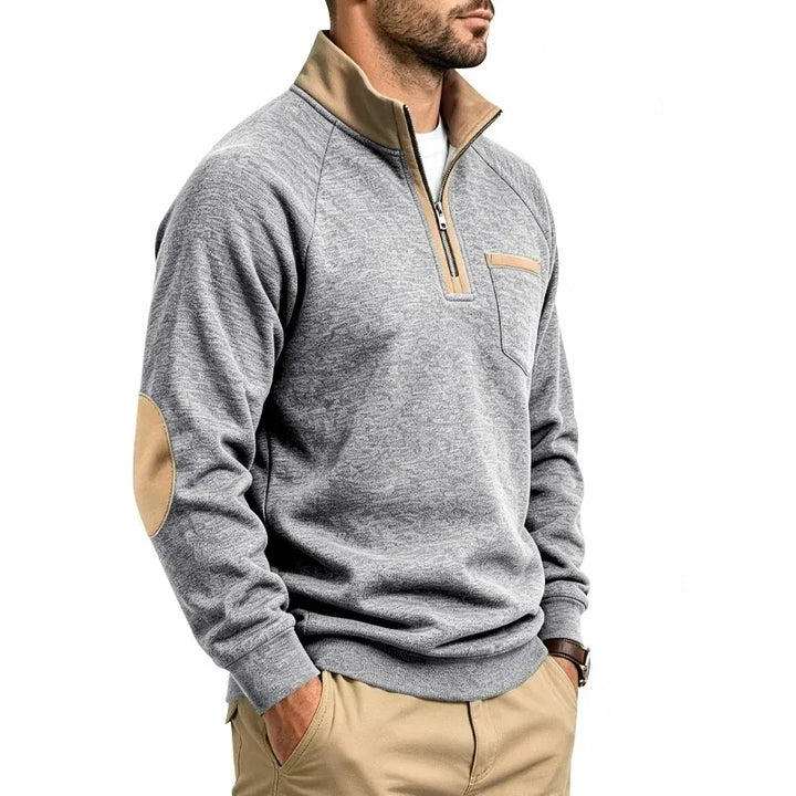 Man wearing a gray melange knit quarter-zip sweatshirt with tan collar lining, chest pocket, and elbow patches.