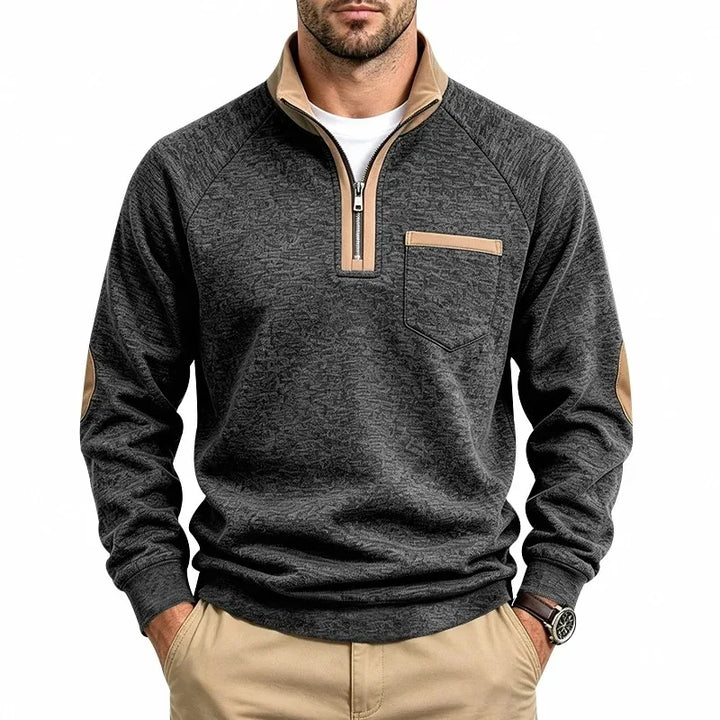 Man wearing a dark gray knit quarter-zip sweatshirt with a tan collar, tan zipper trim, chest pocket, and elbow patches.