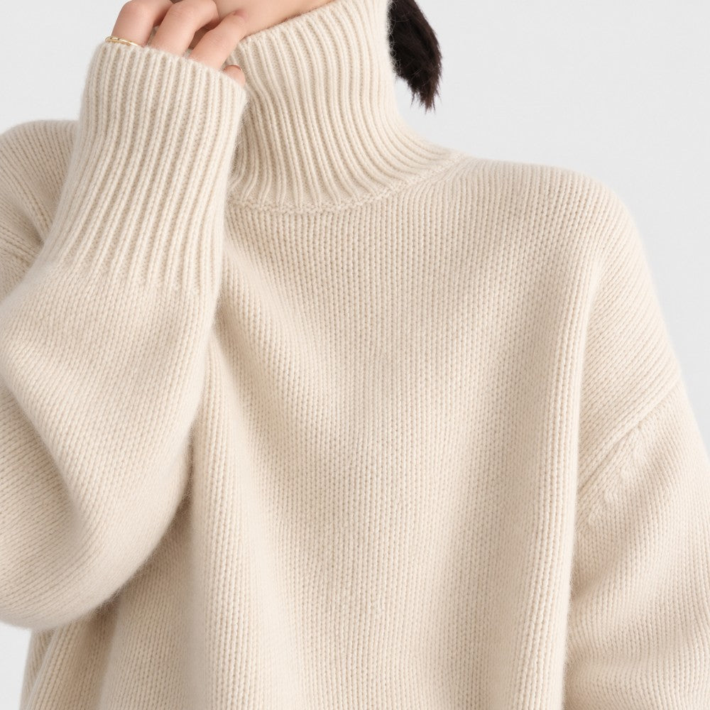 Woman wearing an ivory ribbed-knit turtleneck sweater with dropped shoulders and wide cuffs against a plain white background.