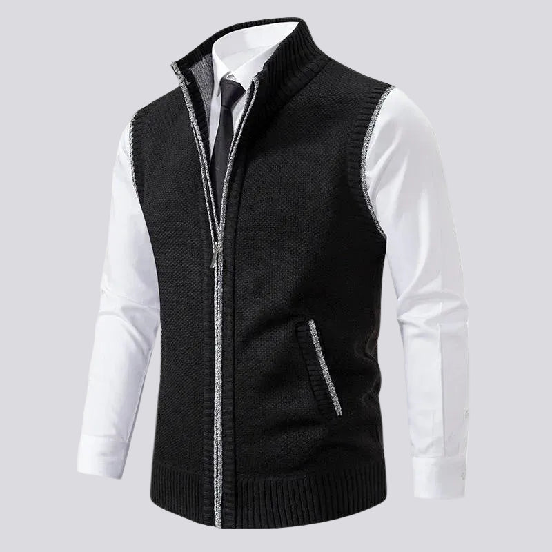 Black knit zip-up vest with a ribbed collar, silver zipper trim, and a small side pocket over a white dress shirt and tie.