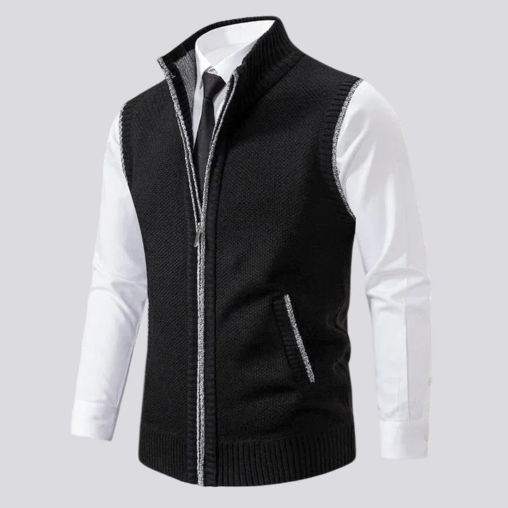 Black knit zip-up vest with a ribbed collar, silver zipper trim, and a small side pocket over a white dress shirt and tie.