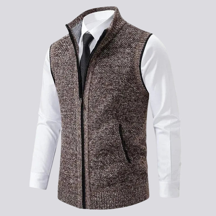 Mannequin wearing a brown flecked knit vest with a black zipper, stand-up collar, and pockets over a white dress shirt and black tie.