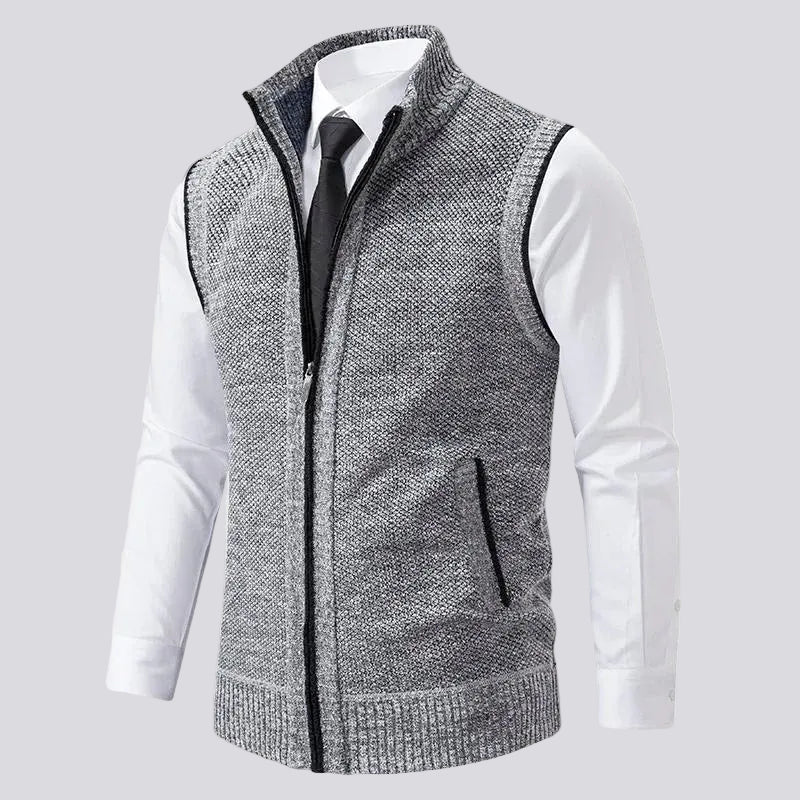 Grey knit vest with a ribbed stand-up collar, black zipper, and two front welt pockets, worn over a white dress shirt and black tie.