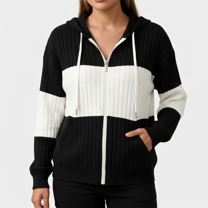 Woman wearing a black and white color-block ribbed knit zip-up hoodie, with her hand in the right front pocket.