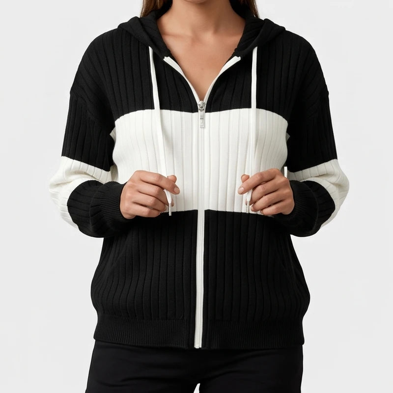 Woman wearing a black and white color block ribbed knit zip-up hoodie, holding the white hood drawstrings.