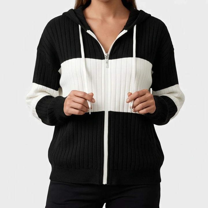 Woman wearing a black and white color block ribbed knit zip-up hoodie, holding the white hood drawstrings.