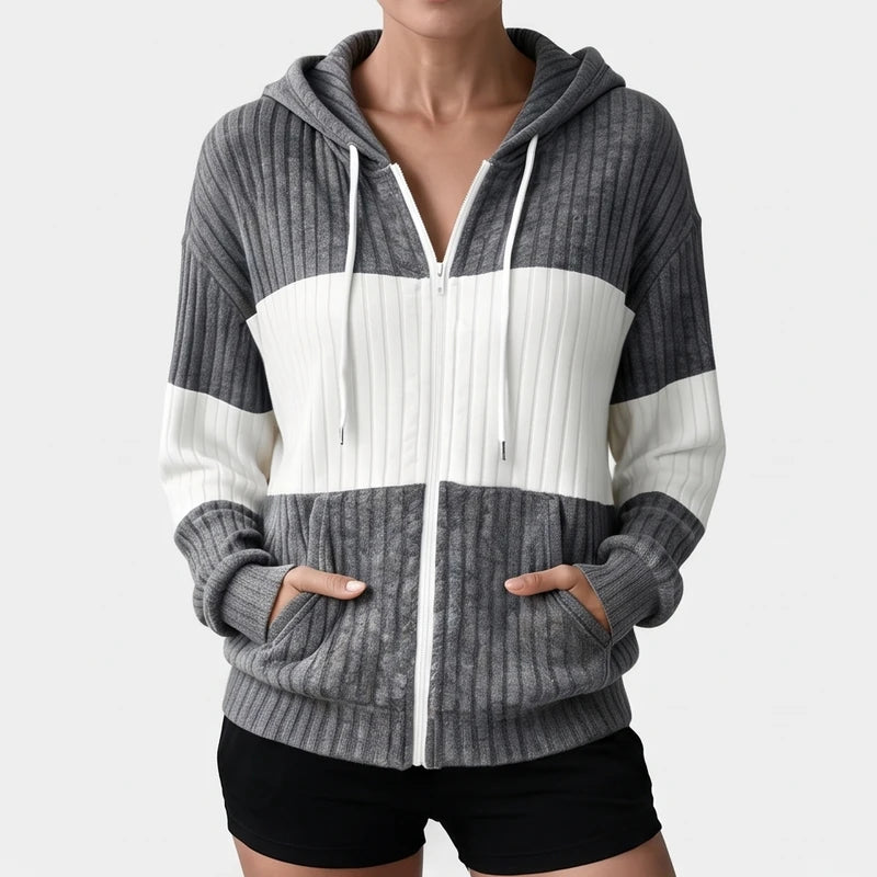 Woman wearing a gray and white color block ribbed knit zip-up hoodie with white drawstrings and front pockets, hands inside pockets.