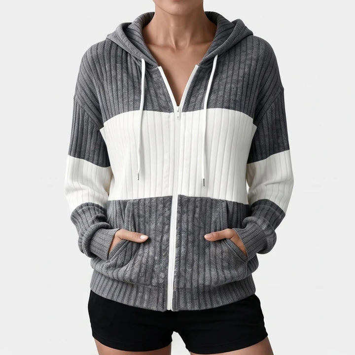 Woman wearing a gray and white color block ribbed knit zip-up hoodie with white drawstrings and front pockets, hands inside pockets.