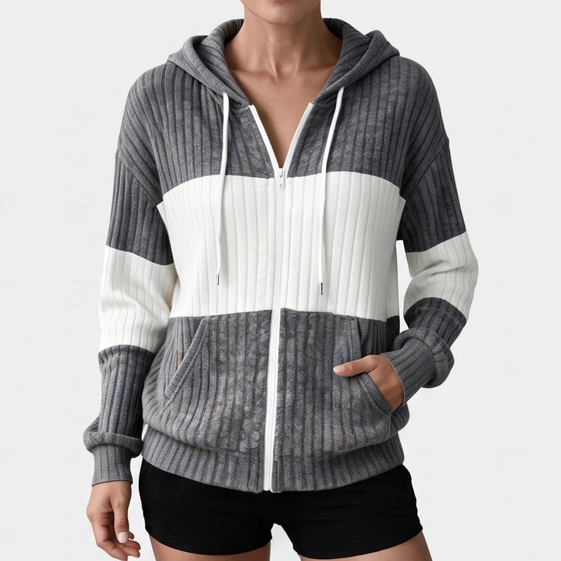 Woman wearing a gray and white striped ribbed knit zip-up hoodie with a white zipper and drawstring, hands in pockets.