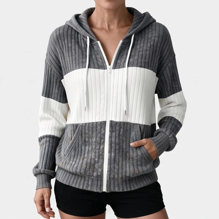 Woman wearing a gray and white striped ribbed knit zip-up hoodie with a white zipper and drawstring, hands in pockets.
