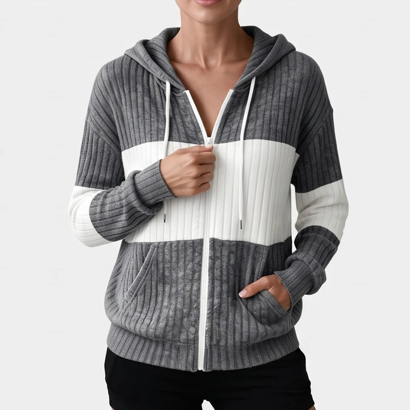 Woman wearing a ribbed knit zip-up hoodie in charcoal gray and white stripes, partially zipped with her hands.