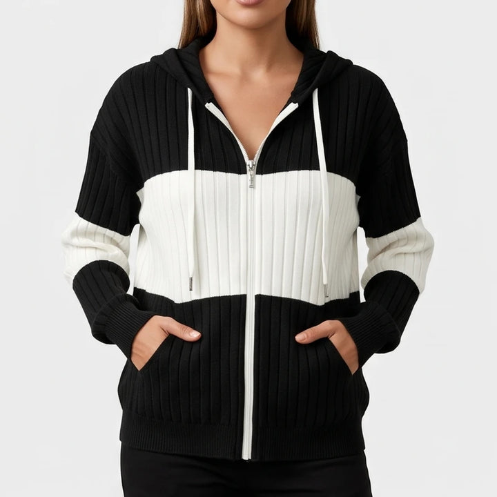 Woman wearing a black and white color block ribbed knit zip-up hoodie with hands in front pockets.