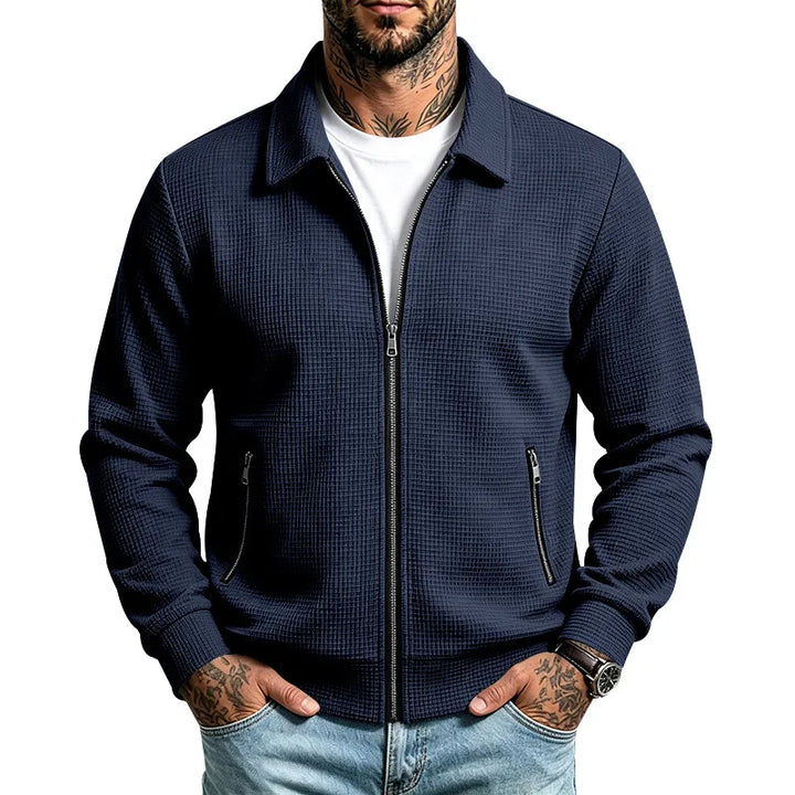 Man wearing a dark blue waffle-knit jacket with a silver front zipper, collar, and side zip pockets.