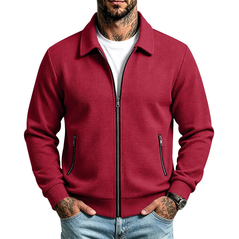 Man wearing a textured red zip-up jacket with a collar, black zippers, and ribbed cuffs and hem, hands in jeans pockets.