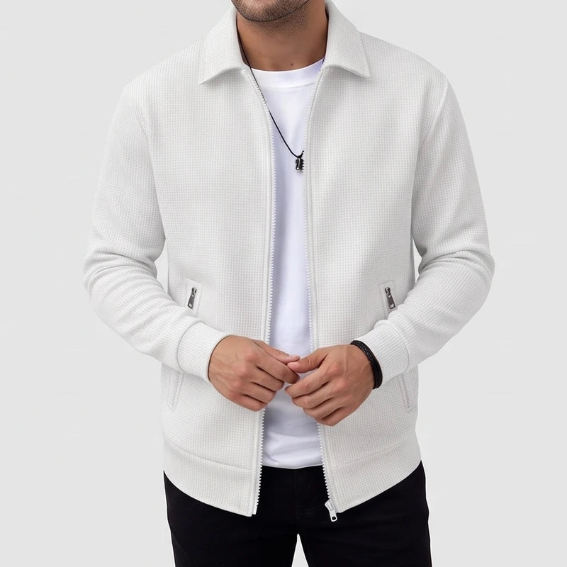 Man wearing an unzipped white waffle-knit jacket with a collar, two zippered pockets, and a dark necklace.