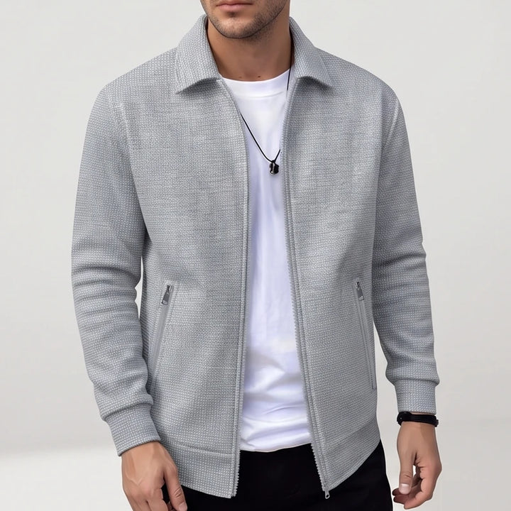 Man wearing a light gray textured knit zip-up jacket with a collar, black zipper, and two side zip pockets.
