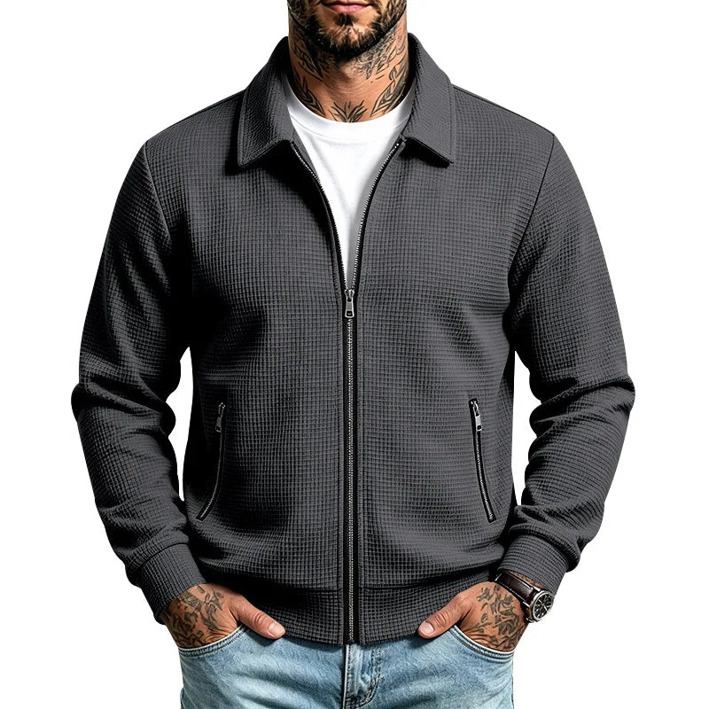 Man wearing a dark grey waffle knit zip-up jacket with a collar, chest partially open over a white t-shirt.