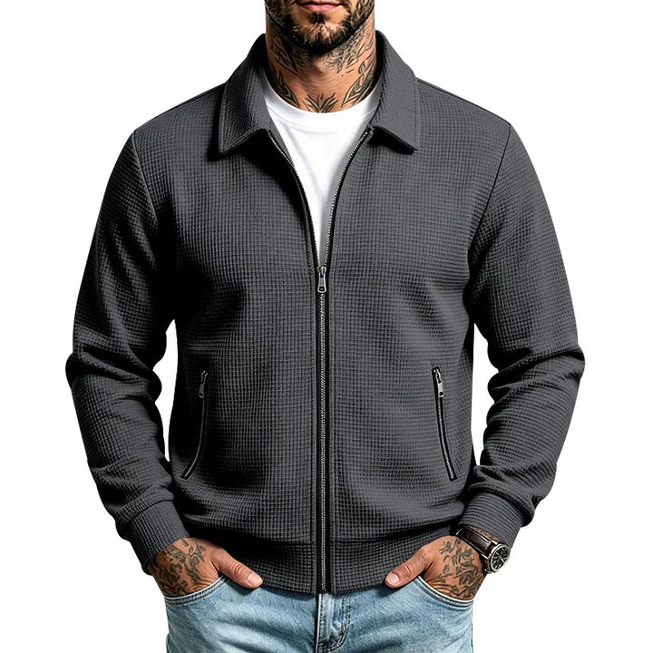 Man wearing a dark grey waffle knit zip-up jacket with a collar, chest partially open over a white t-shirt.