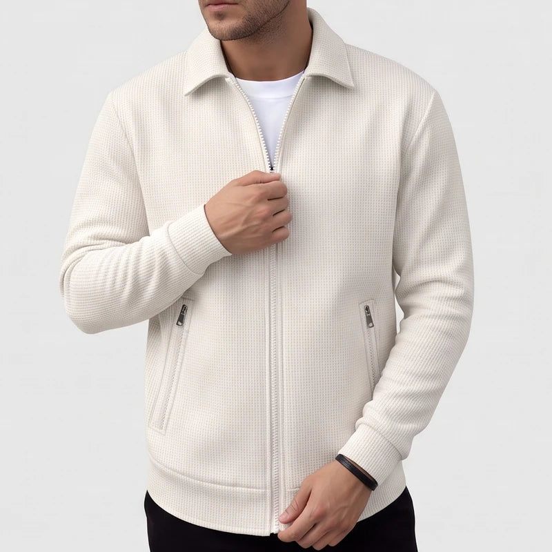 Man wearing a cream waffle-knit jacket with a collar, full zipper, and two zippered pockets, adjusting the zipper.
