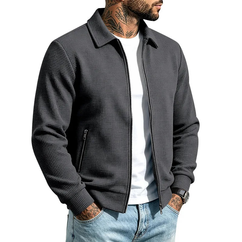 Man wearing a dark gray waffle knit jacket with a collar, visible front zipper, and zippered side pocket.