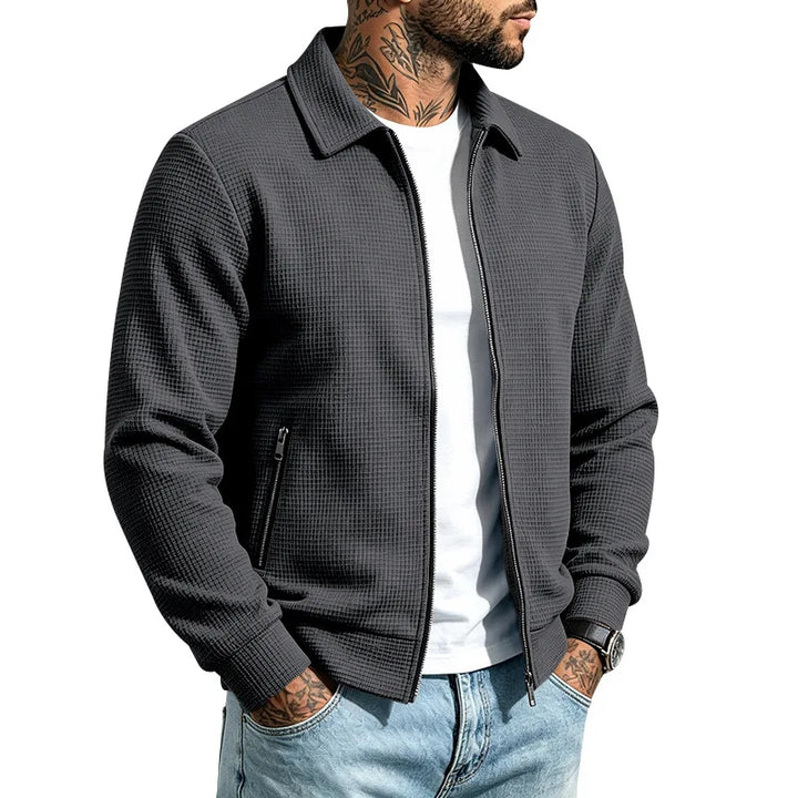 Man wearing a dark gray waffle knit jacket with a collar, visible front zipper, and zippered side pocket.